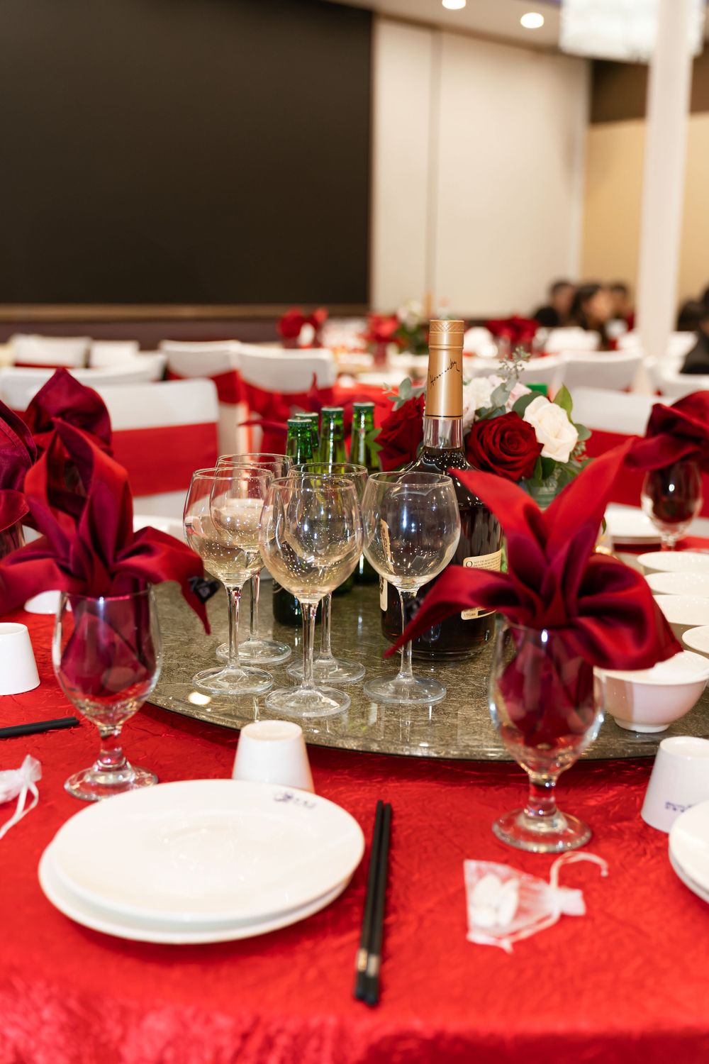 Elegant wedding reception table setting with red tablecloth, wine glasses, and deep red floral centerpieces.