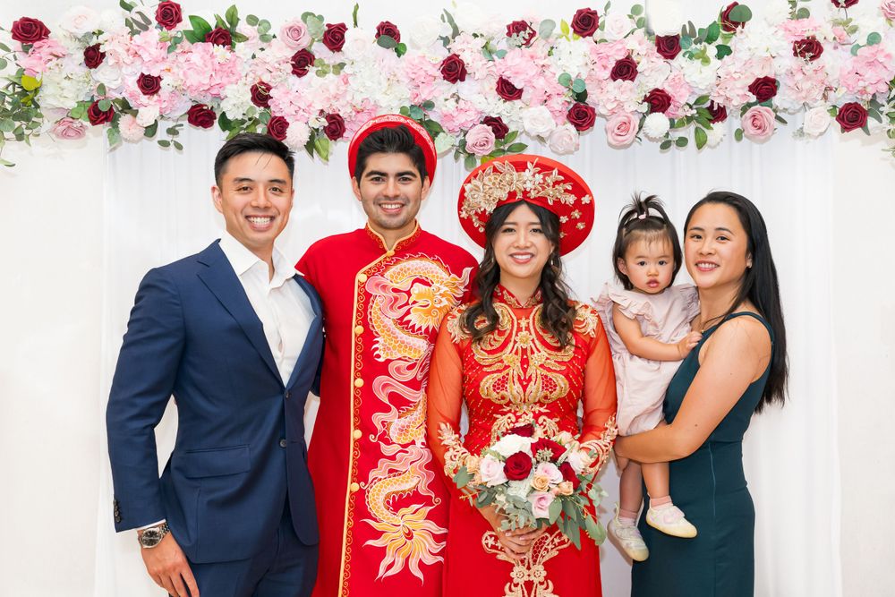Family group photo at wedding with traditional Vietnamese bride and groom under floral arch.