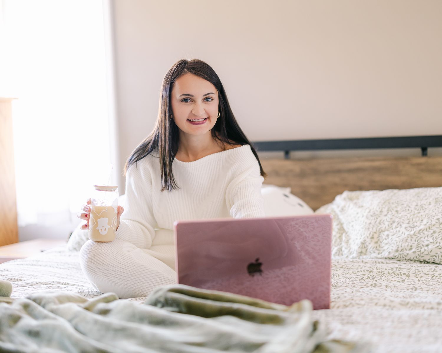 Person relaxing in bed with laptop and coffee while working from home.