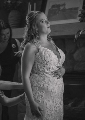 Close-up of the bride's dress being buttoned by her mother, captured in timeless black and white.