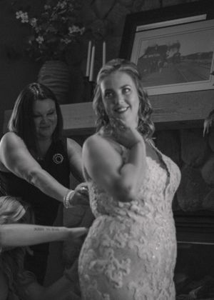 Close-up of the bride's dress being buttoned by her mother, captured in timeless black and white.