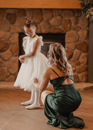 Member of bridal party assisting a girl in the wedding party with her dress, creating a heartfelt moment of support.