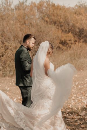 Bride and groom walking together, with the bride playfully adjusting her veil.