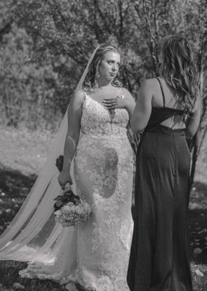 Bridesmaid and bride sharing an intimate moment, captured in striking black and white.