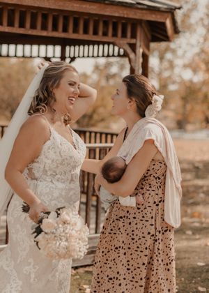 Bridesmaid and sister sharing a joyful moment, with sister holding her newborn.