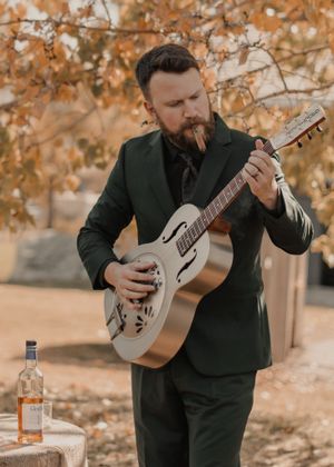 Groom playing a new guitar gifted by the bride, enjoying a moment of relaxation with a cigar.