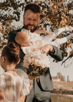 Groom playfully lifting his daughter in the air, capturing a fun and joyful moment between father and daughter.