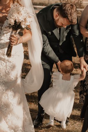 Groom dancing with his daughter, reaching down joyfully for a playful moment outside.