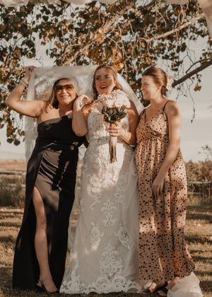 Bridal portrait of bride, mother, and sister posing together with a delicate veil, showcasing their fun bond.