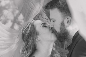 Bride and groom share a kiss, with a trendy veil elegantly framing the background of this romantic moment.