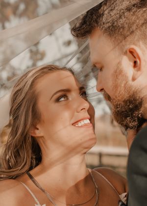 Bride gazes lovingly at groom, with a trendy veil elegantly framing the background.