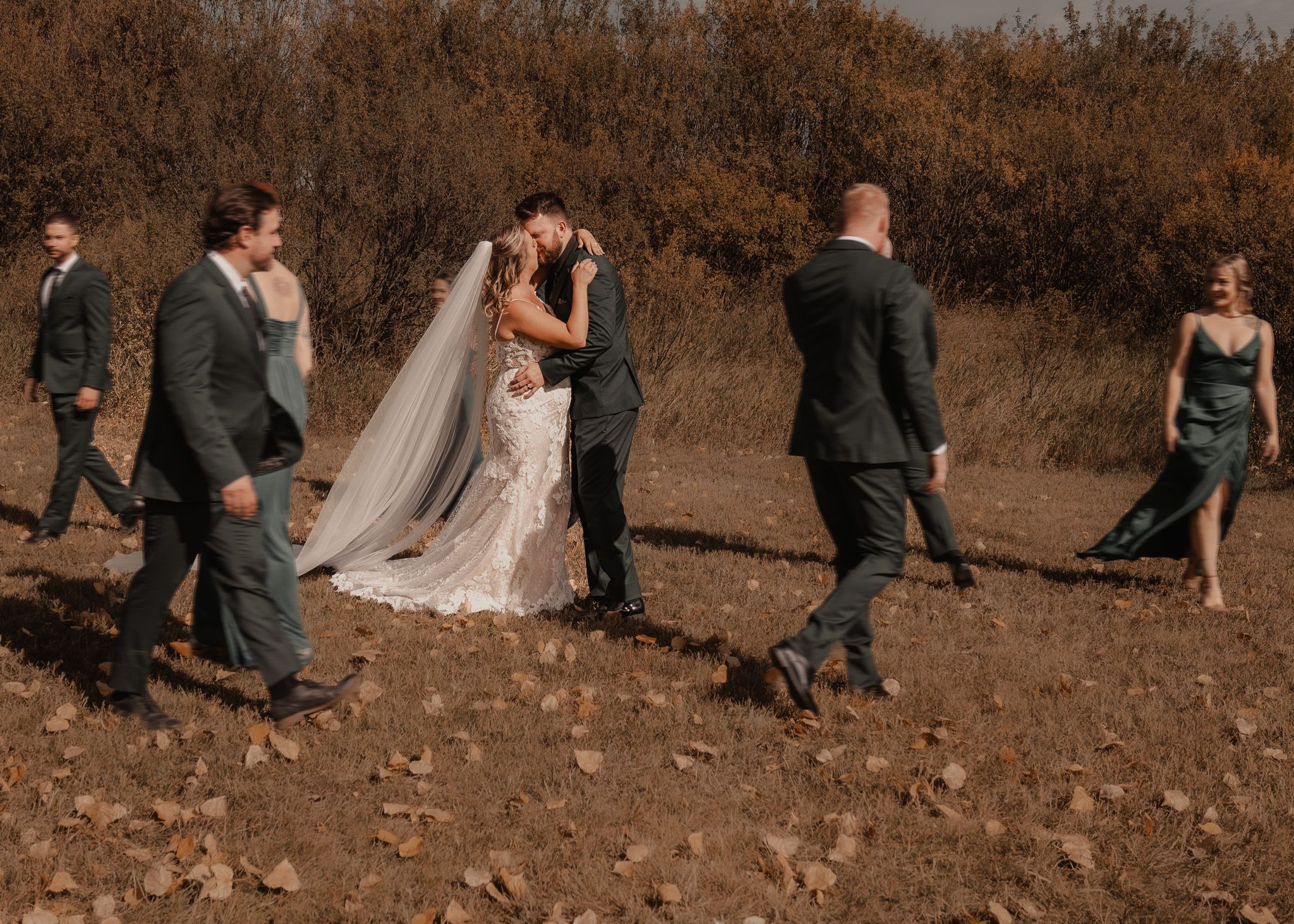 Trendy blurred shot of a wedding party walking around a couple, captured in warm fall tones.