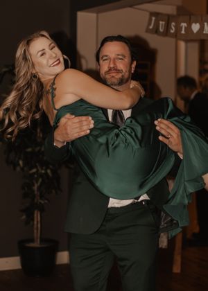 Couple in wedding party, male lifting female off the floor in a playful moment.