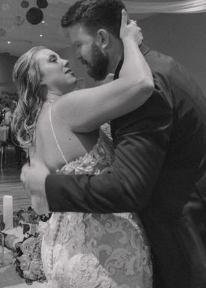 Candid embrace of bride and groom about to kiss as guests clink glasses.
