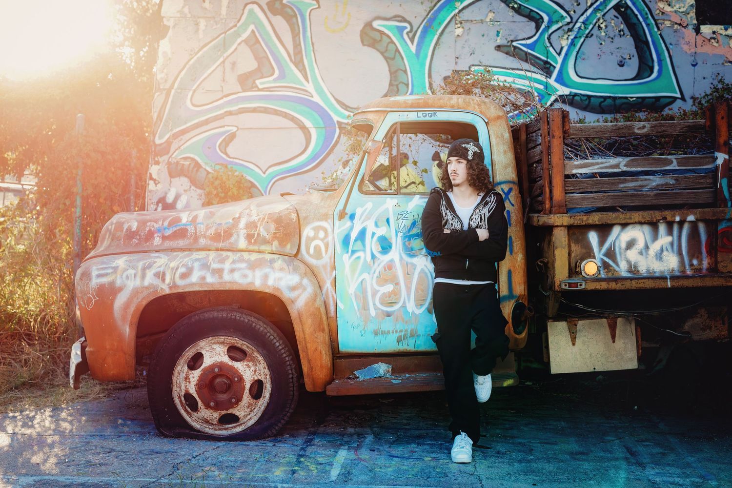 A stylish pose against a vintage truck covered in graffiti art during golden hour.