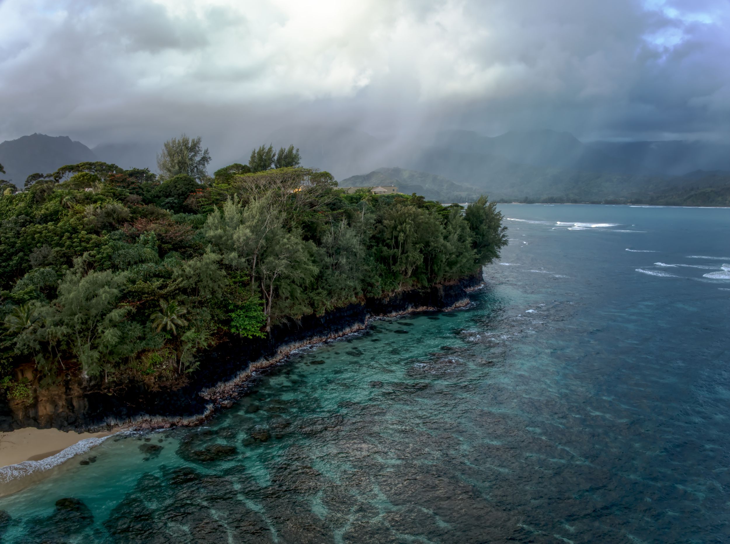Beautiful Beach in Hawaii with rain clouds over a green forest.