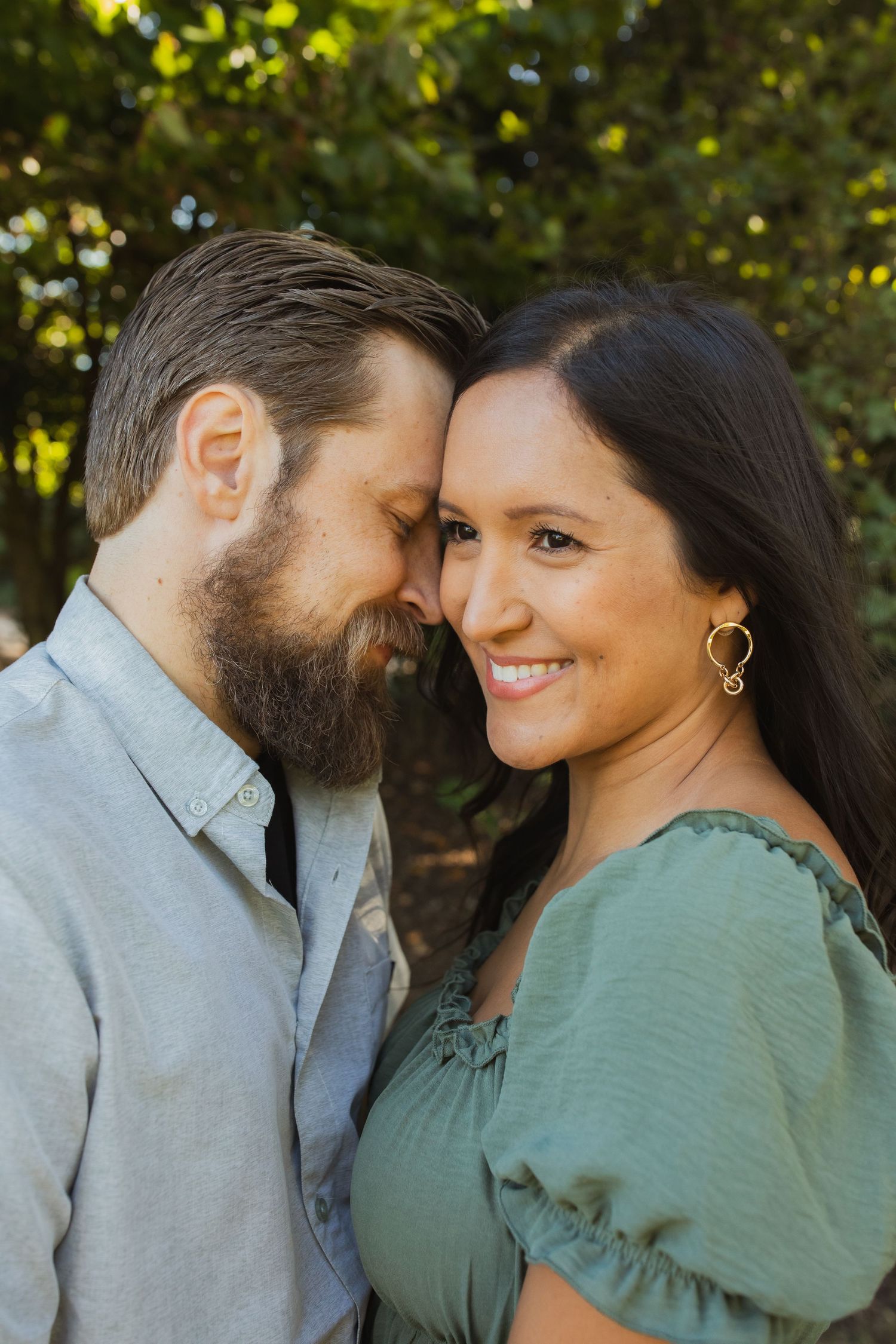 Couple in casual attire sharing an intimate moment against a sunlit natural backdrop.