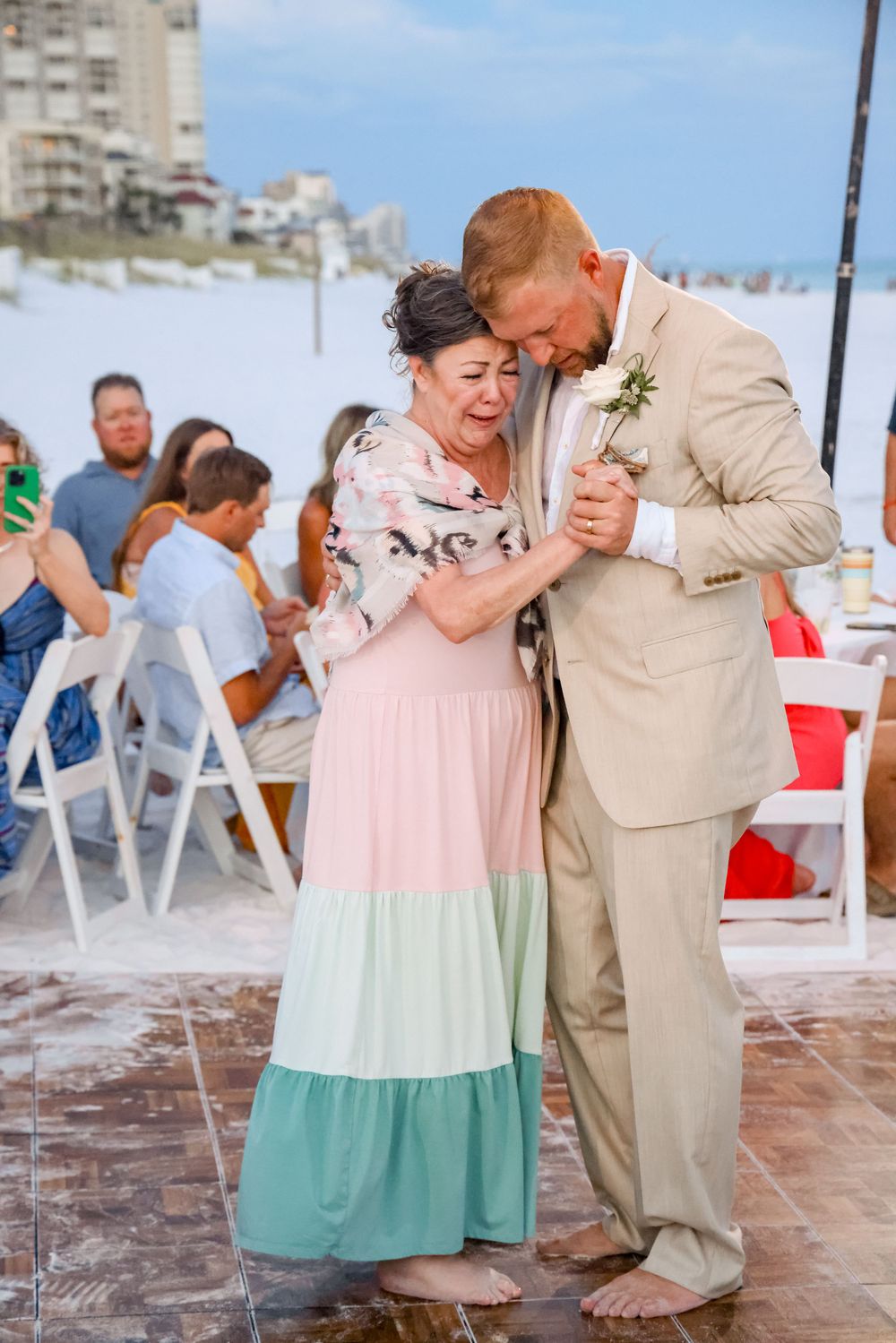 A couple shares a joyful dance moment at a beach wedding wearing a pink ombré dress and tan suit.