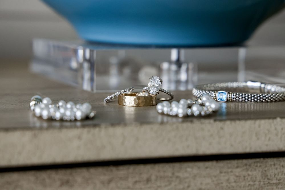 Wedding rings and jewelry arranged elegantly on neutral surface.