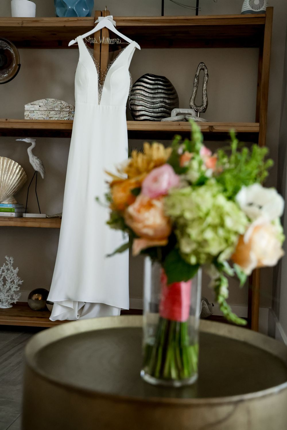 Elegant white wedding dress hanging beside fresh flower bouquet on wooden shelving.