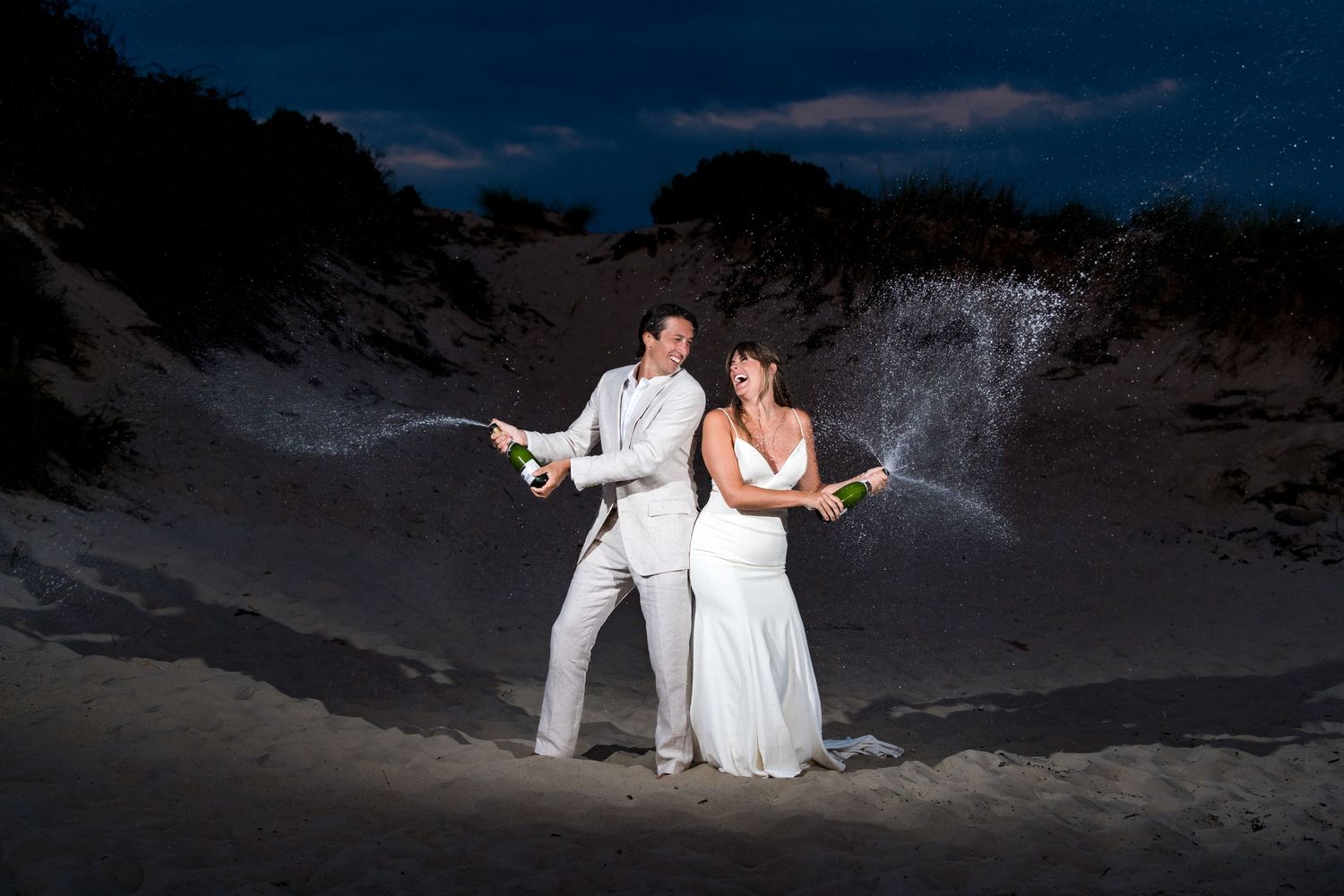 A wedding ceremony takes place on a scenic coastal bluff at sunset with greenery and ocean views in the background.
