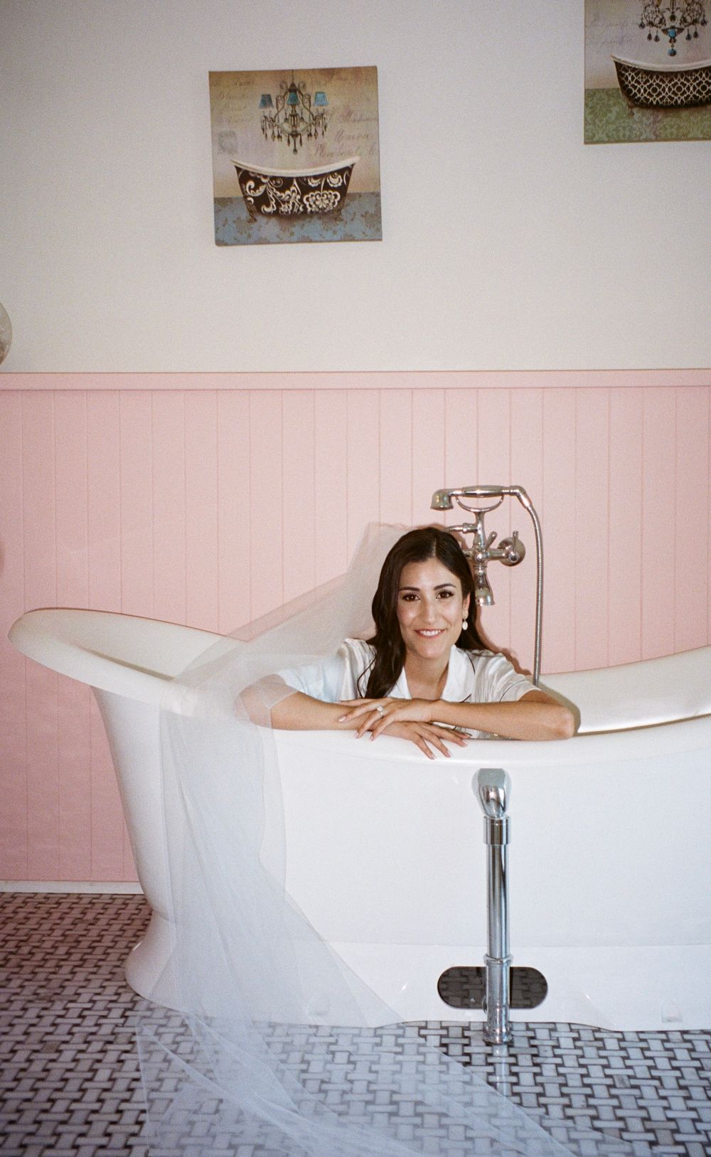 Elegant clawfoot bathtub against pink wainscoting with vintage bathroom decor.