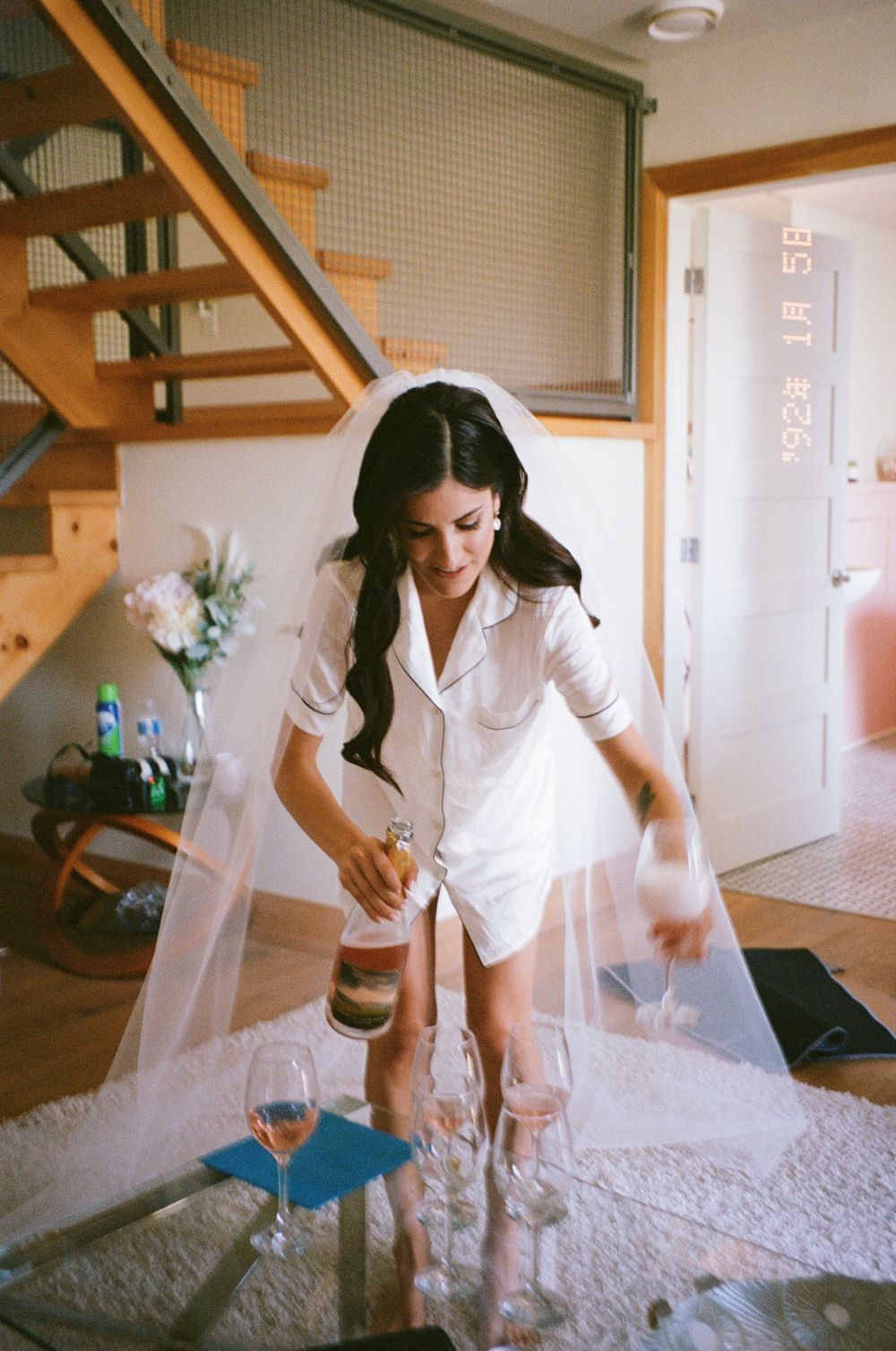 White bridal preparation moment in a sunlit room with wooden stairs.