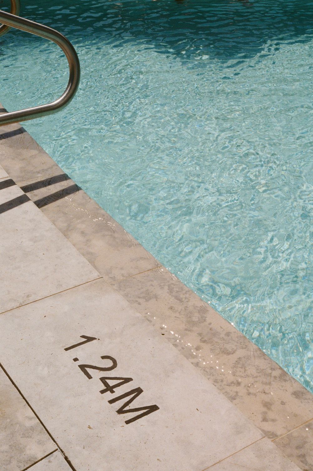 Corner of swimming pool showing depth marker 7.2M and crystal clear turquoise water.