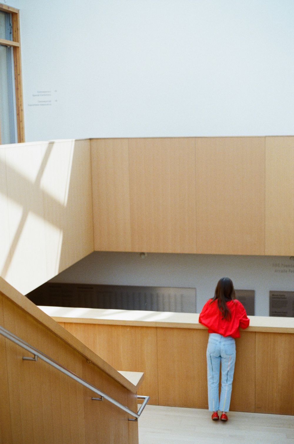 Person in red sweater and jeans looking over modern wooden interior balcony.