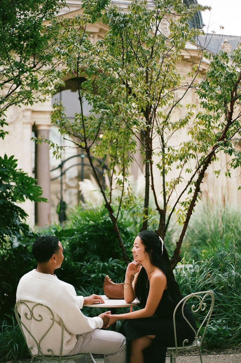 Two people engaged in conversation on vintage garden chairs surrounded by greenery.