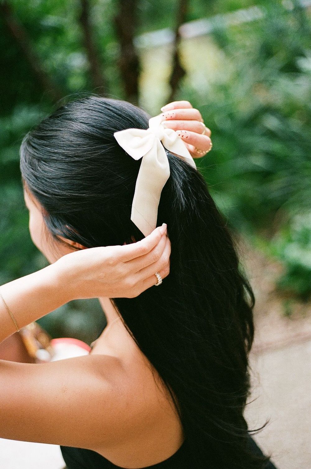 Close up of hands adjusting white bow in long dark hair outdoors.