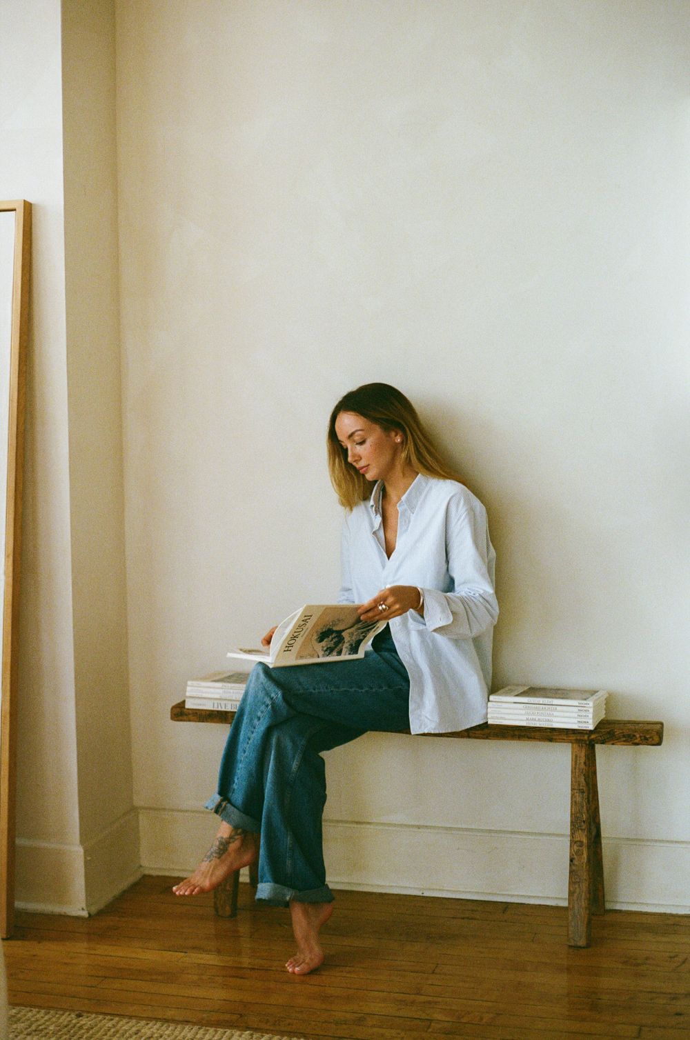 Casual lifestyle scene of person reading book while sitting barefoot on wooden bench.