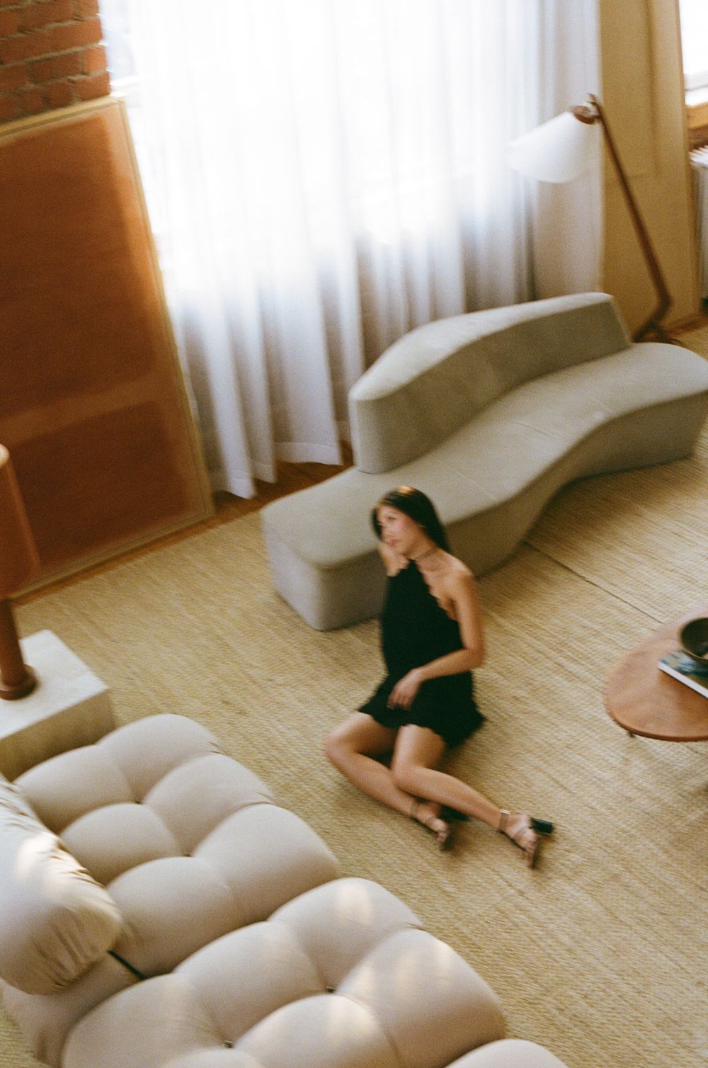 A woman in a black dress relaxes on a modern white sectional sofa in a minimalist room.
