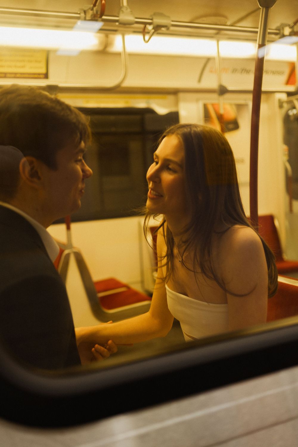 A romantic couple shares an intimate moment while sitting in a dimly lit subway car.