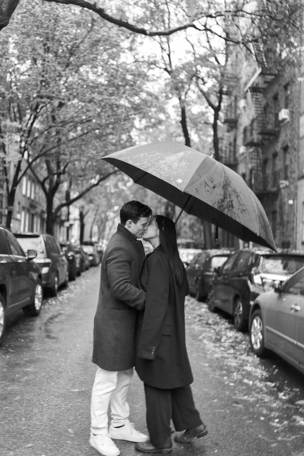 A couple shares a romantic moment under an umbrella on a rainy city street.