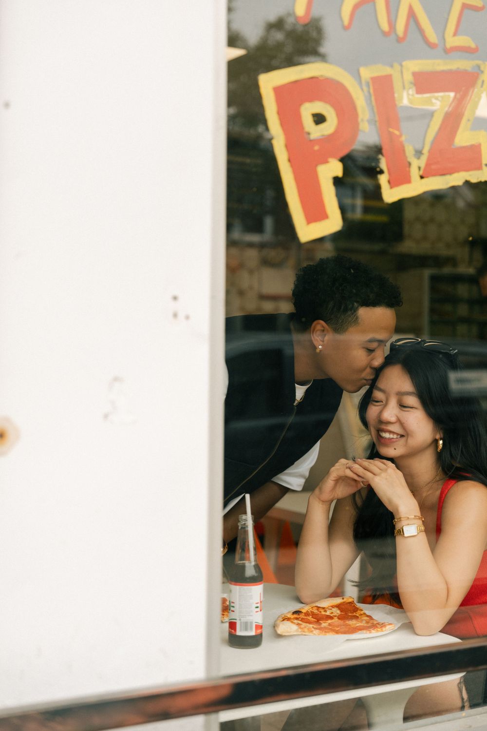 A couple enjoys a romantic moment at a pizza restaurant with a pizza on the table.