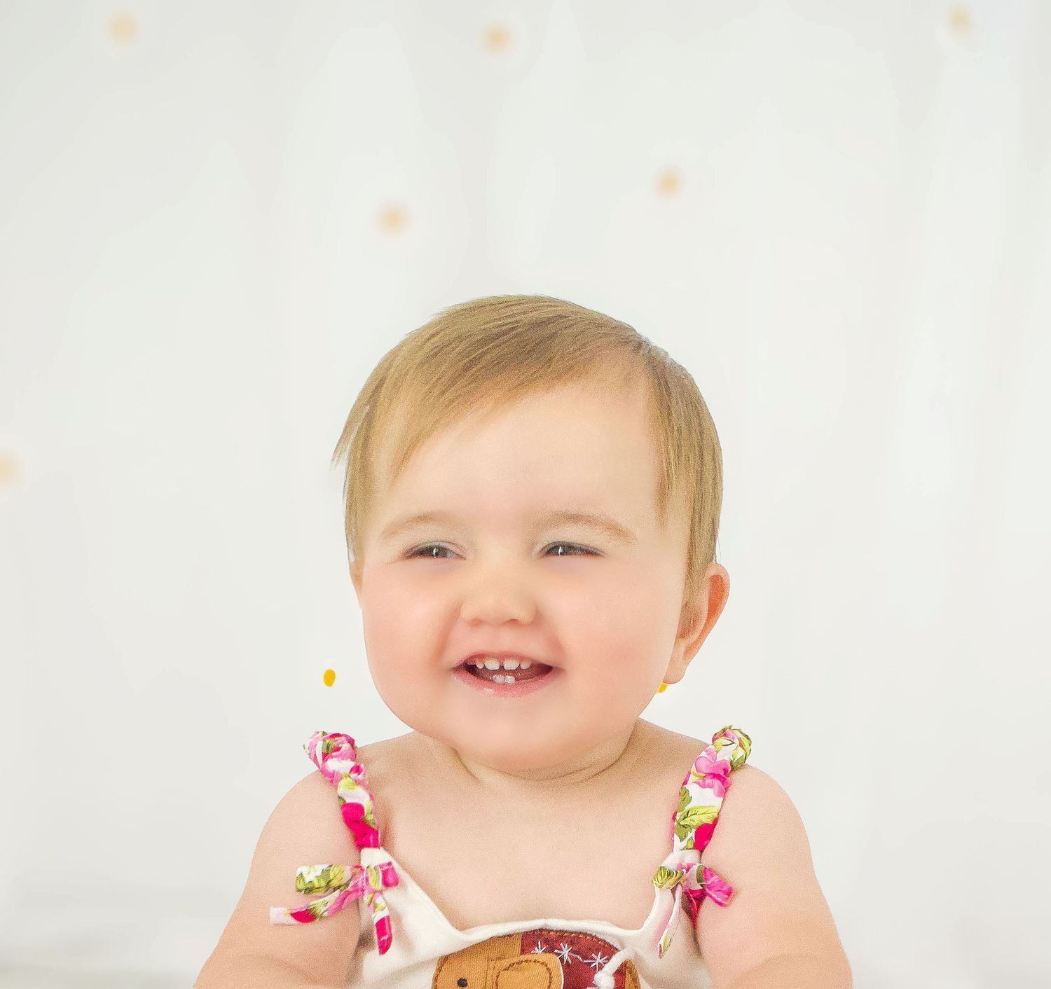 Young child in pink floral dress smiling and playing against white backdrop.