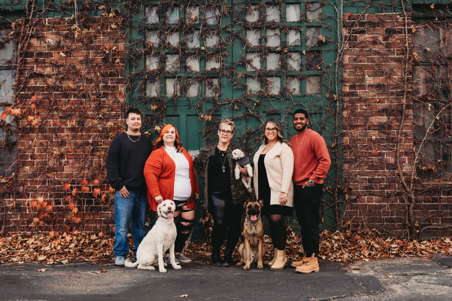 Group portrait with dogs against rustic brick wall with industrial metal grid.