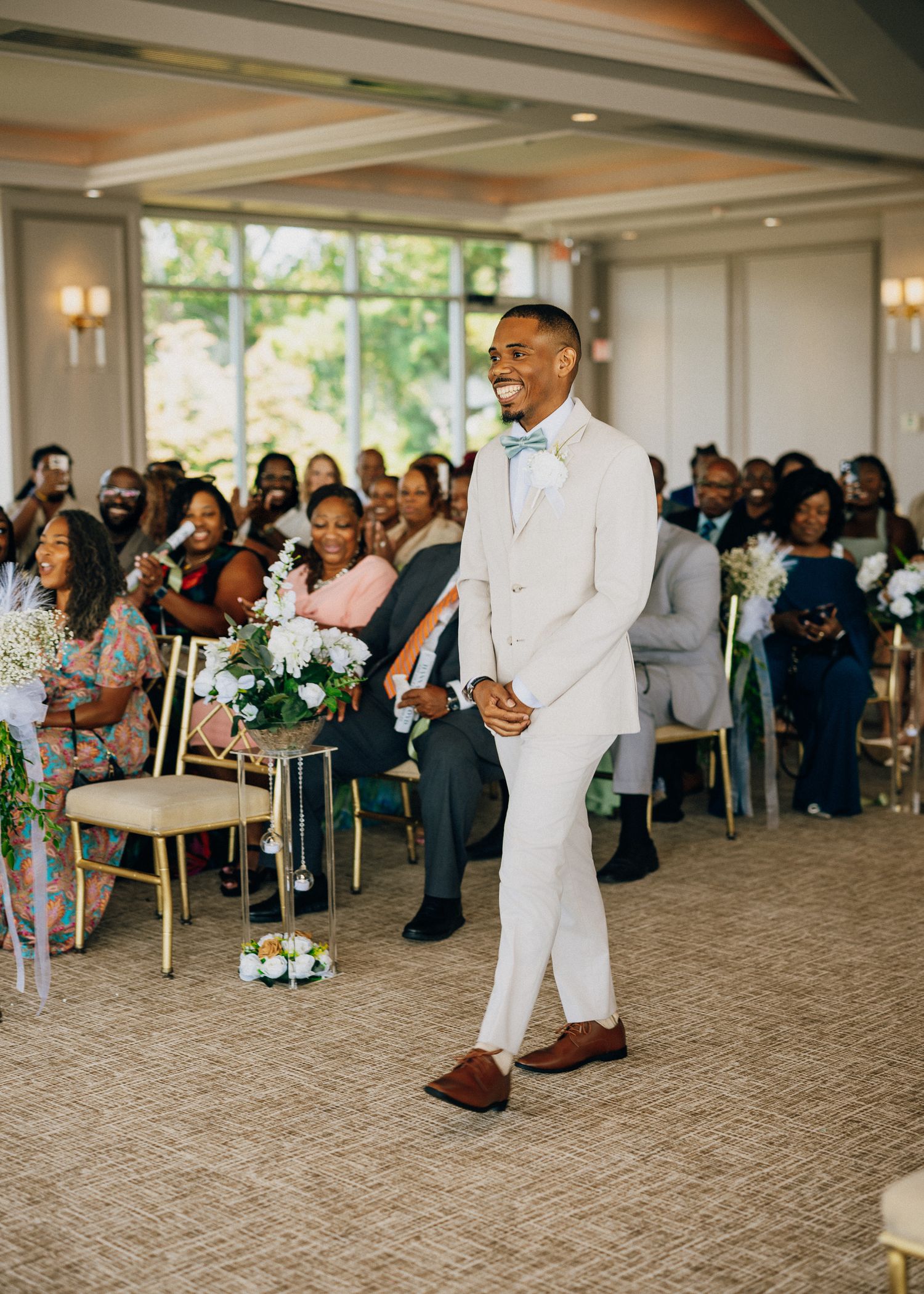 Wedding party members perform a joyful dance line across a carpeted reception venue floor during celebration.