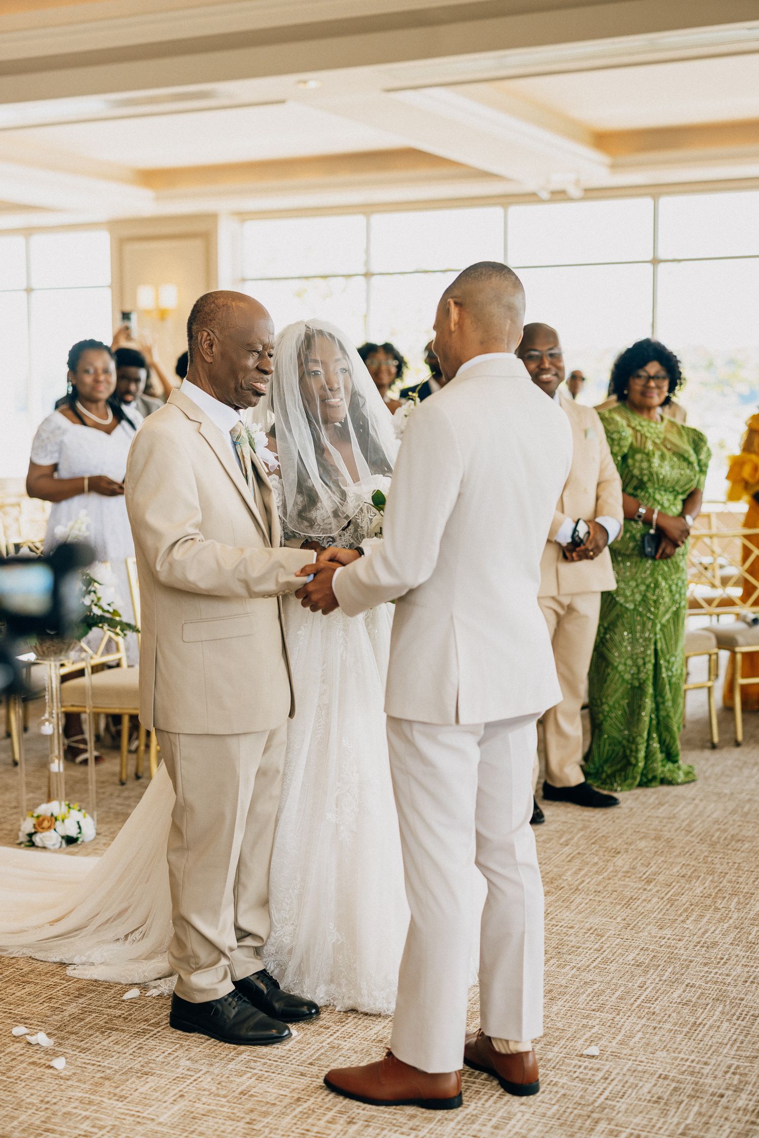 Wedding guests in cream-colored formal attire dance together on a carpeted ballroom floor during a celebration.