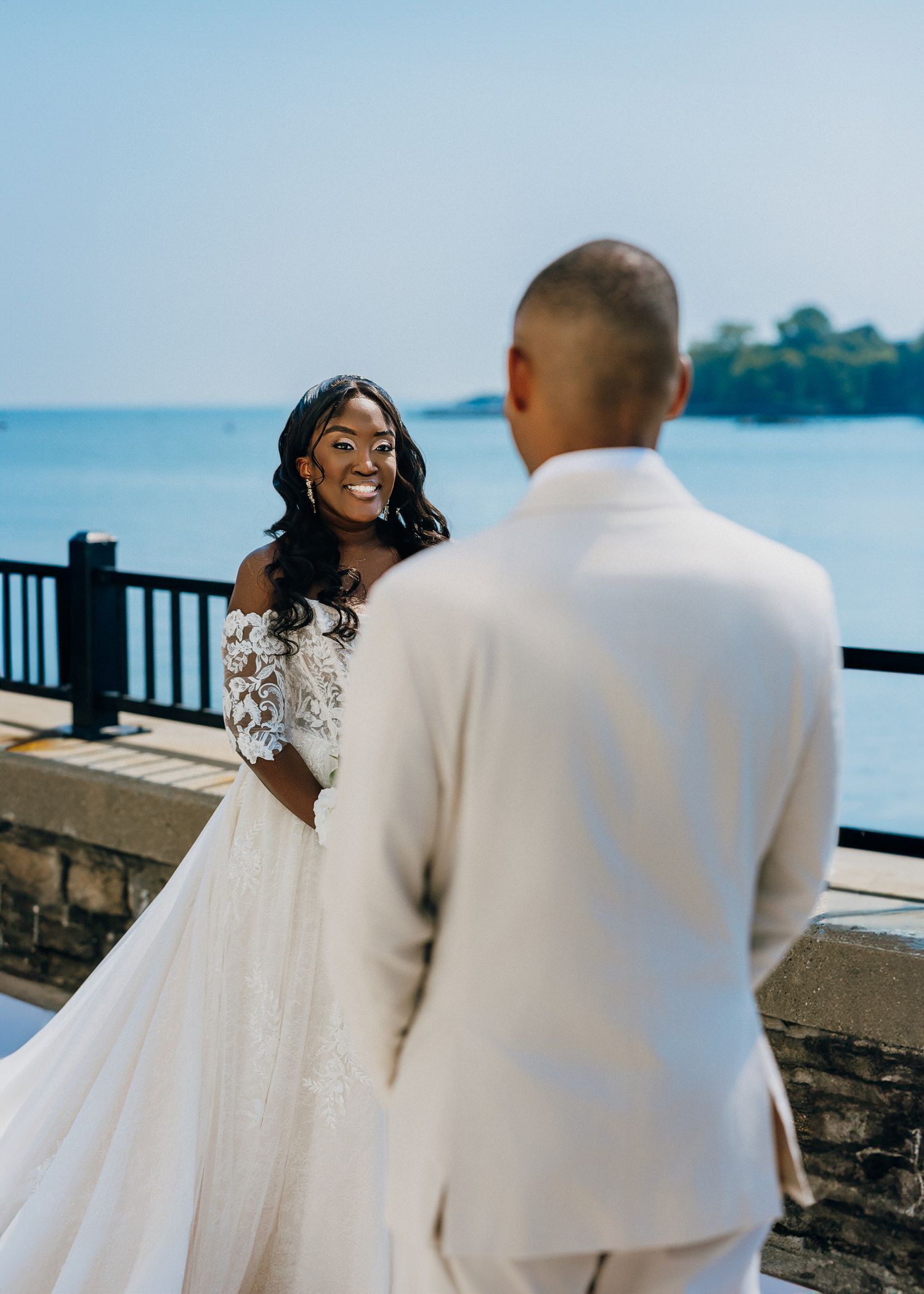 A couple in white attire shares romantic moments by a waterfront pier on their wedding day.