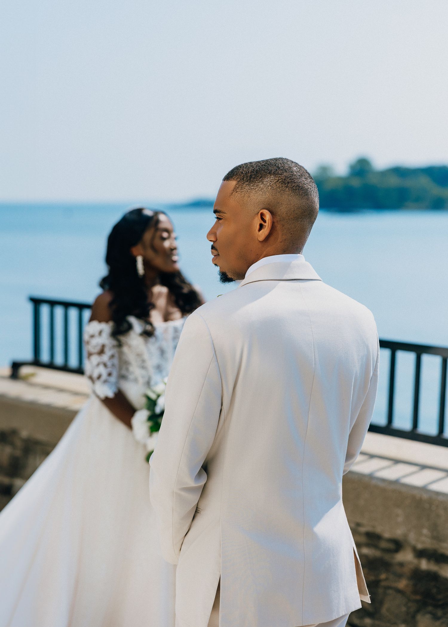 A couple in white outfits shares a romantic moment by the waterfront railing during a photo session.