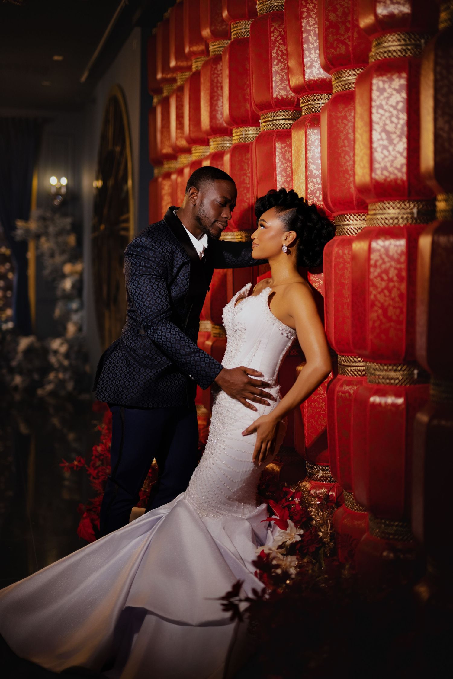 A couple shares a romantic moment in front of a vibrant red wall during their wedding photoshoot.