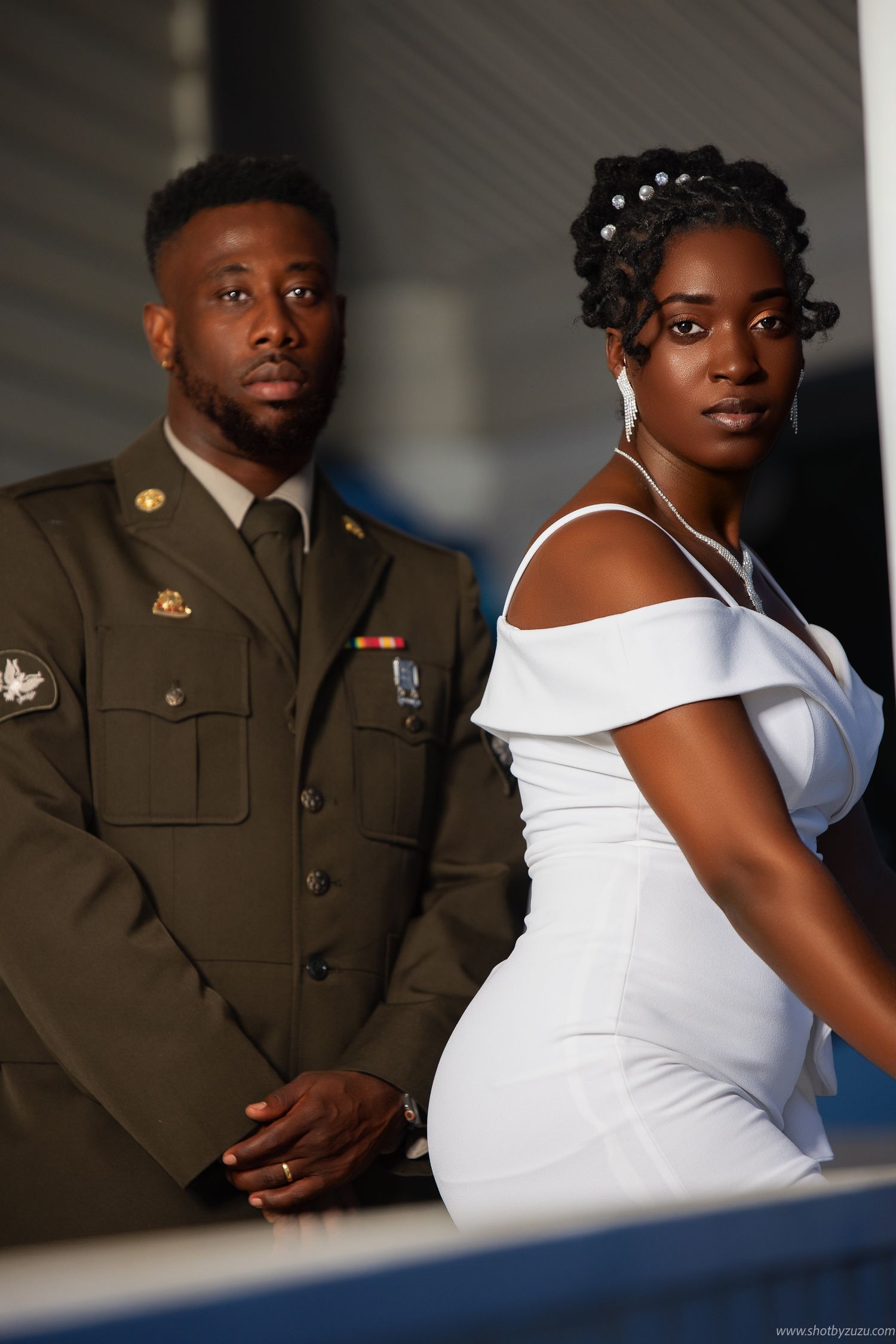 A military service member and bride pose for a formal portrait in dress uniform and white gown.