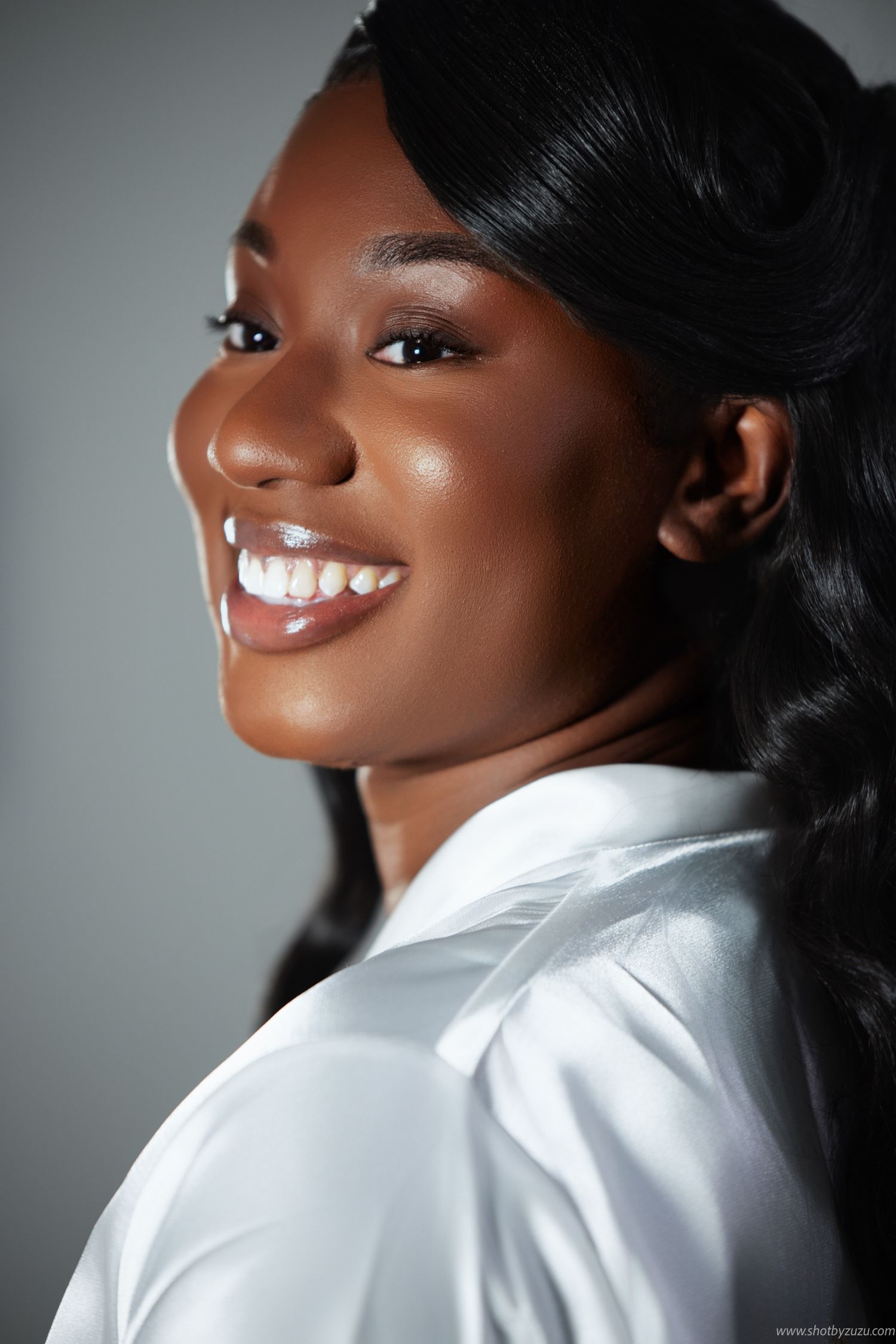 Side profile portrait showing elegant makeup and joyful smile against grey background.