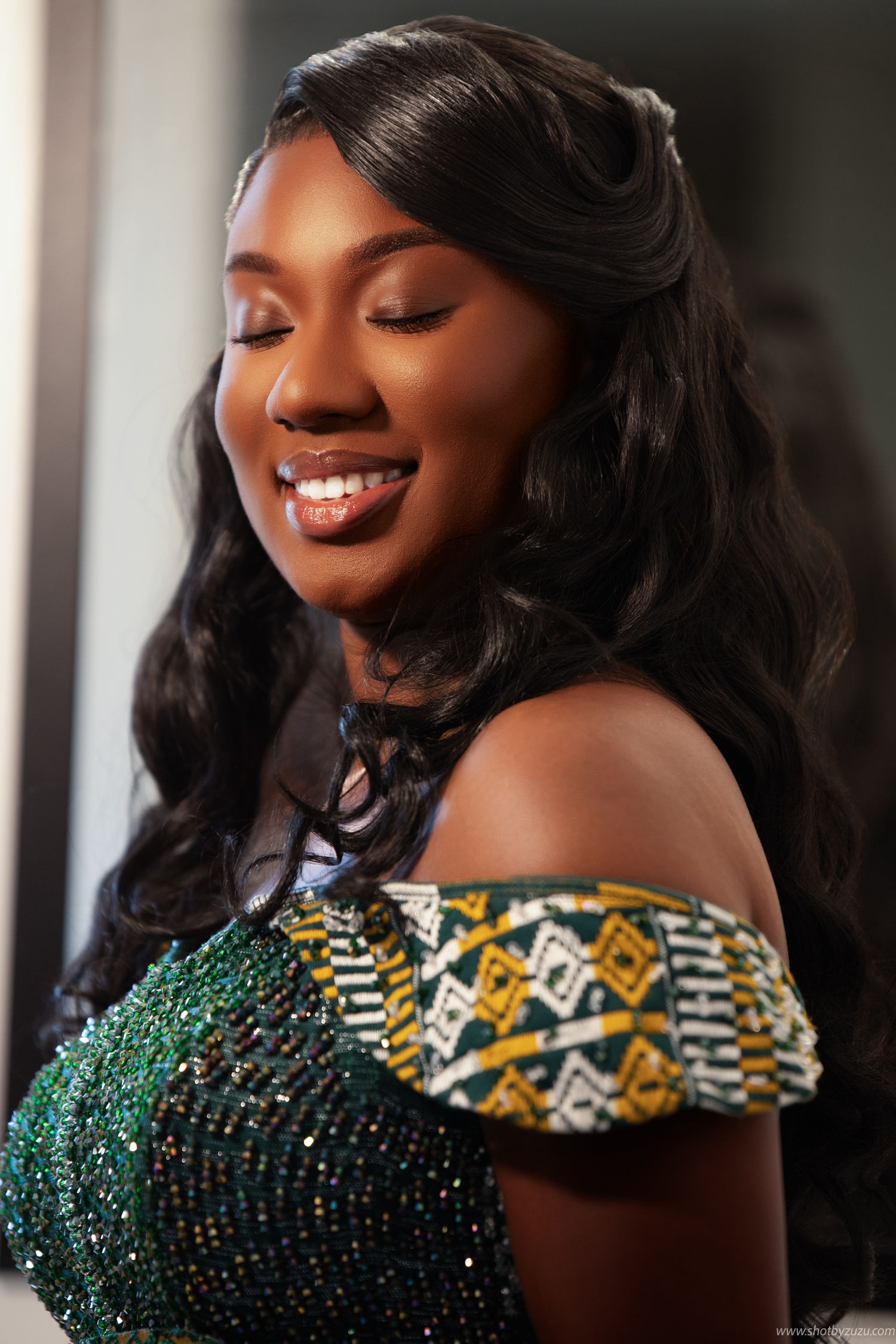Formal portrait showing off-shoulder emerald green dress with traditional African print details.