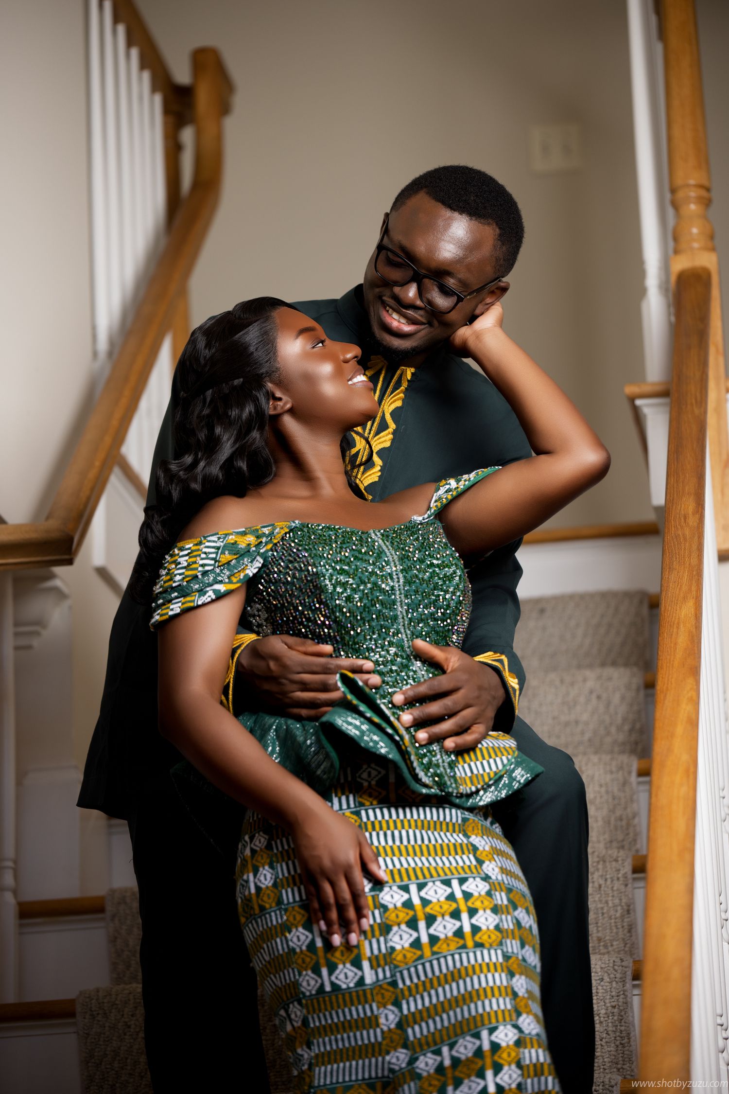Couple in formal African attire share intimate moment on staircase.