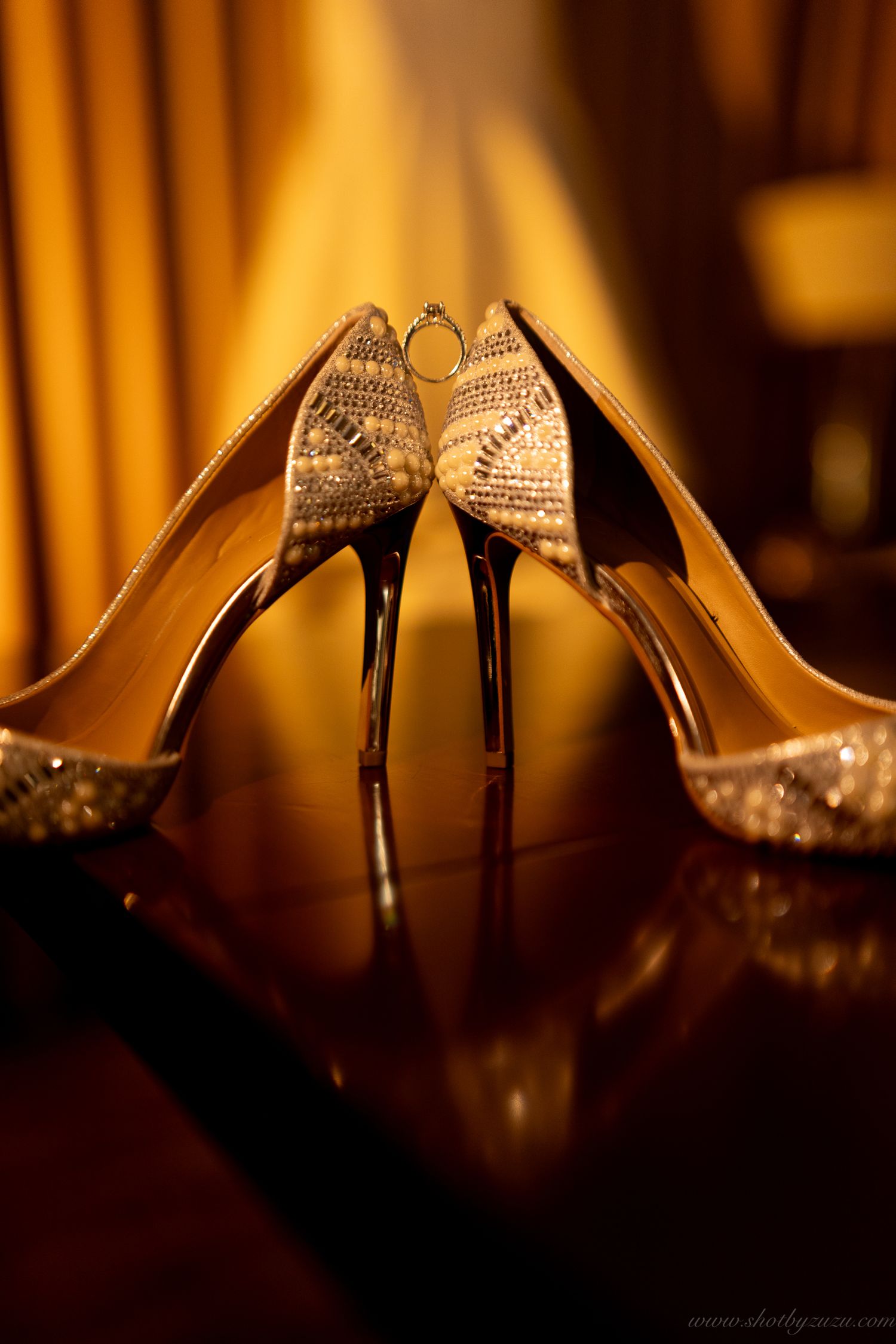 Crystal-embellished wedding heels positioned artistically on reflective surface with warm lighting.