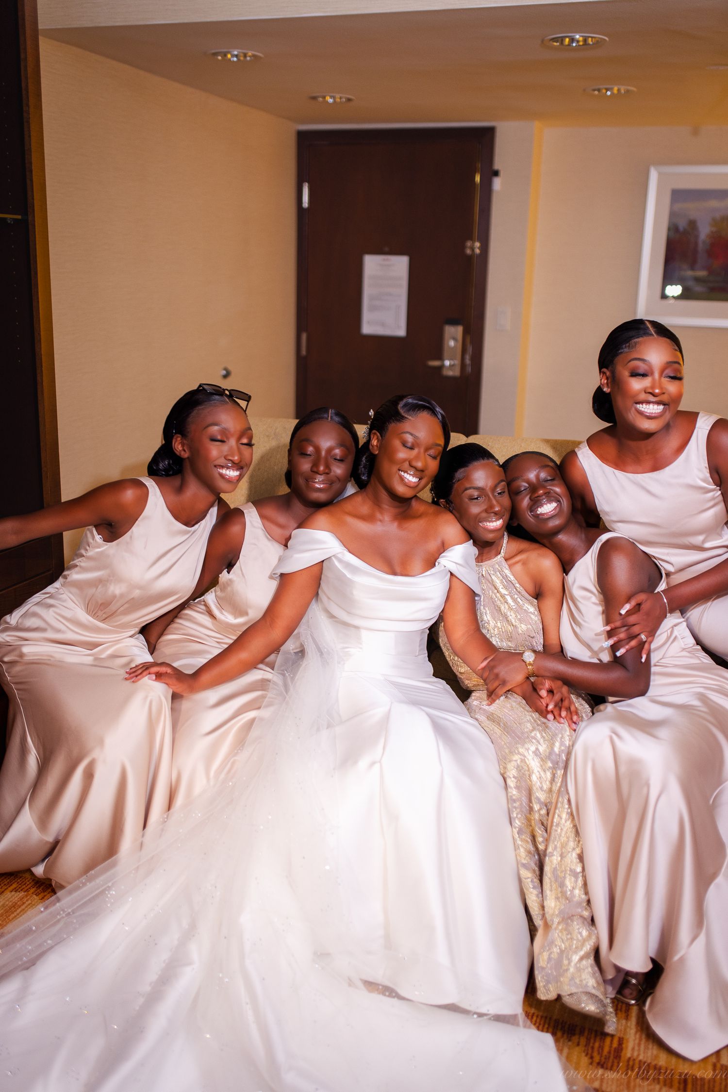 Joyful bridal party in matching cream dresses share laughs while sitting together.