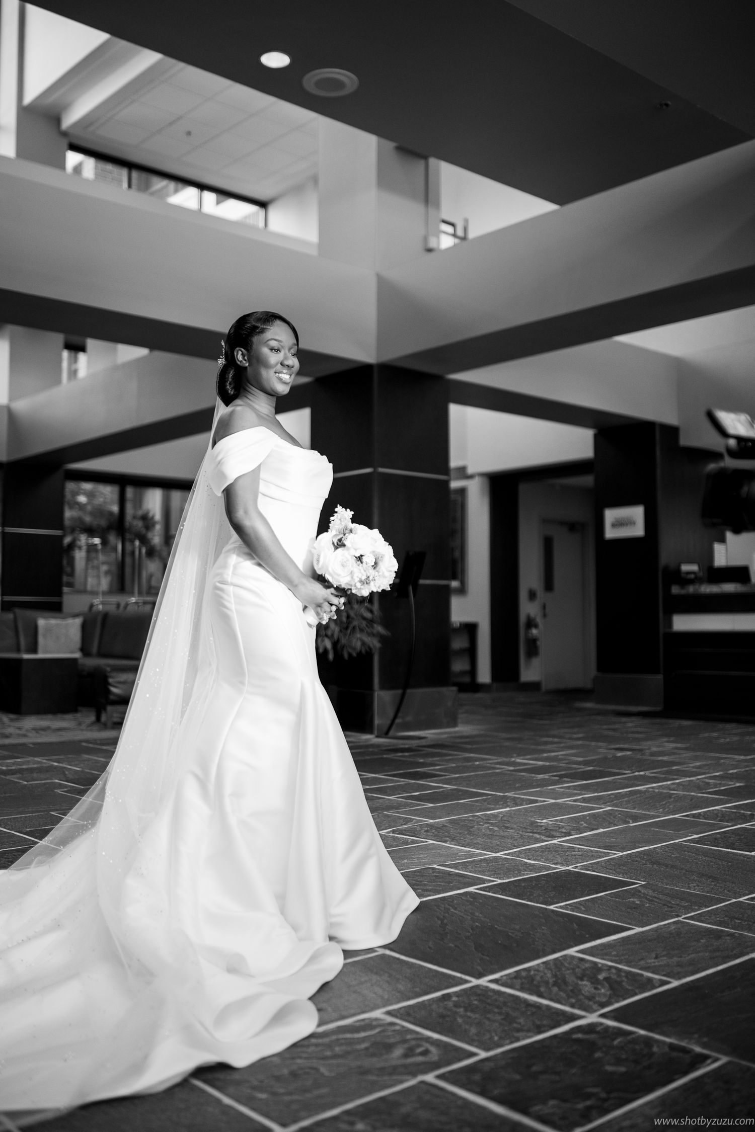 An elegant bride in a white gown holds a bouquet while posing in a black and white photograph.